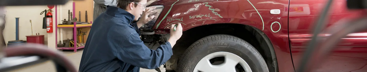 Body shop employee marking dents on the front fender of a damaged vehicle.